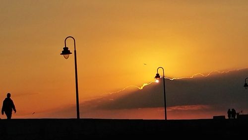 Silhouette people on street light against orange sky