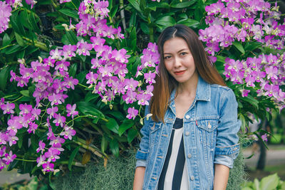 Portrait of smiling young woman standing by flowering plants