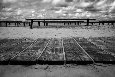 Empty bench on pier at beach against sky
