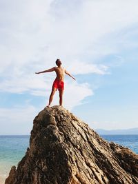 Shirtless man standing on rocky shore against sky