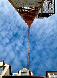 Low angle view of crane by building against sky