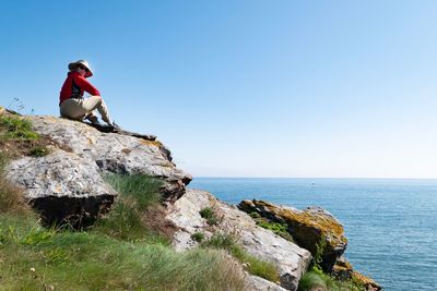 Man sitting on rock by sea against sky