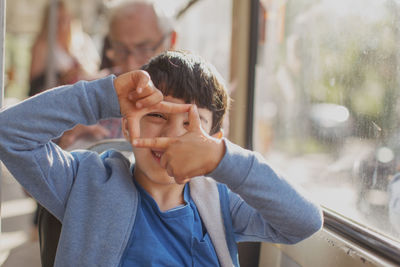 Portrait of boy looking through finger frame in bus