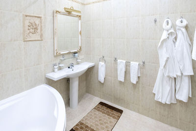 Bathroom with white sink and toilet, white bathrobes for guests hang the wall.