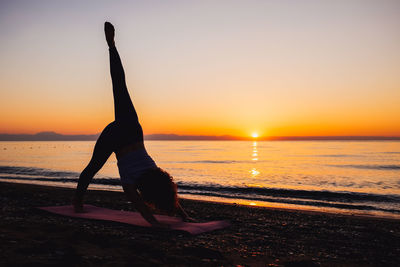 Silhouette woman standing on beach against sky during sunset