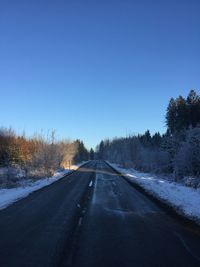 Road amidst trees against clear blue sky during winter