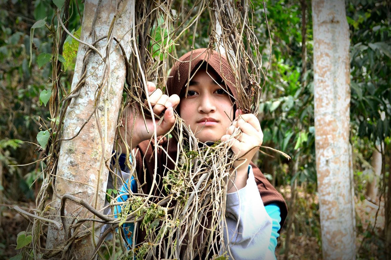 person, tree, portrait, looking at camera, forest, lifestyles, leisure activity, casual clothing, tree trunk, front view, smiling, young adult, childhood, elementary age, standing, three quarter length, happiness, girls