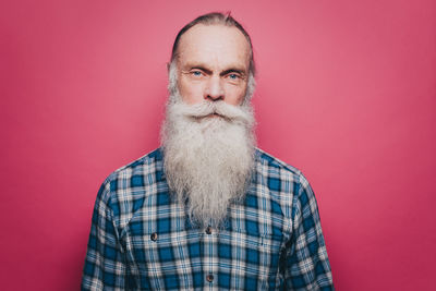 Portrait of confident senior man with long white beard against pink background