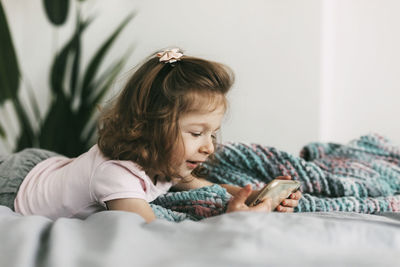 A little girl watches cartoons on her phone or plays on the bed before going to bed