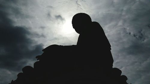 Low angle view of silhouette man sitting against sky