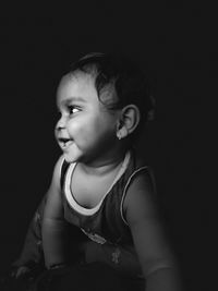 Cute baby girl looking away against black background