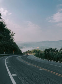 Empty road by trees against sky