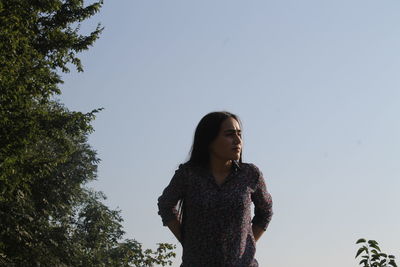 Young woman looking away while standing against clear sky