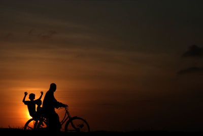 Silhouette people riding bicycle against sky during sunset