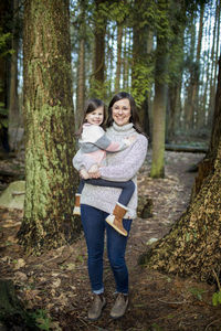 Mother holding her cute little girl in the forest.