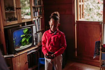 Positive black teen girl in casual clothes with joystick controller in hands playing in room with wooden interior and old fashioned tv