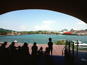 People looking at river by cityscape against sky