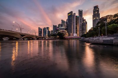 Bridge over river by buildings against sky during sunset