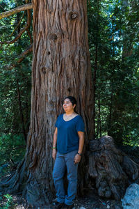 Full length of smiling man standing on tree trunk in forest