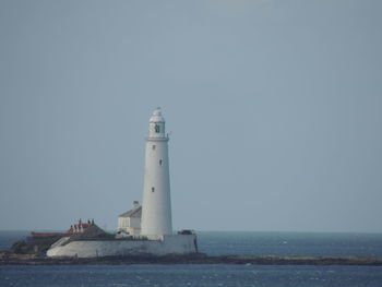 Lighthouse by sea against clear sky