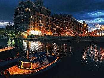 Illuminated boats moored in river against sky at night