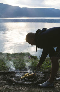 Man preparing corn by lake on barbecue 