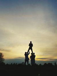 Silhouette friends forming human pyramid against sky during sunset