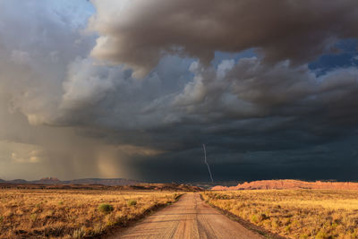 A dirt road leading to dark, ominous storm clouds and lightning in southern utah