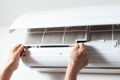 Cropped hands of man cleaning air conditioner on wall