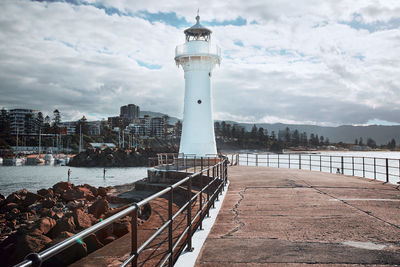 Lighthouse at harbor against cloudy sky