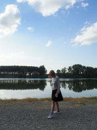 Rear view of woman standing by lake against sky