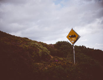 Road sign on field against sky