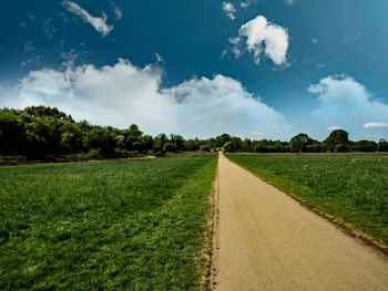 Empty road amidst field against sky