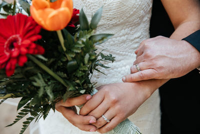 Midsection of woman holding flower bouquet. bride and groom's hands with rings close up