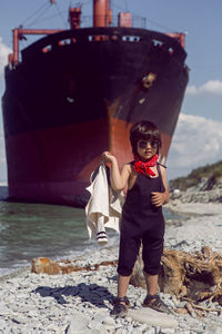 Fashionable boy child with long hair stand on a log next to a large ship that ran, near novorossiysk