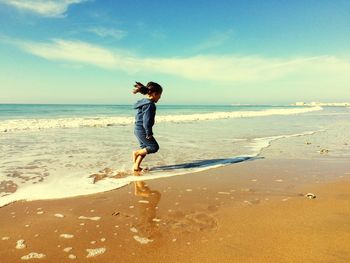 Full length of playful girl running on shore at beach against sky during summer