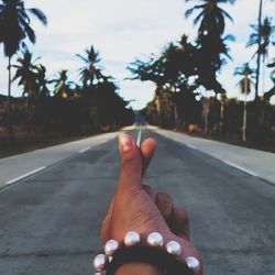 Close-up of woman hand while gesturing on road by trees against sky