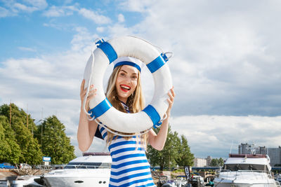 Young woman standing on yacht posing with lifebuoy