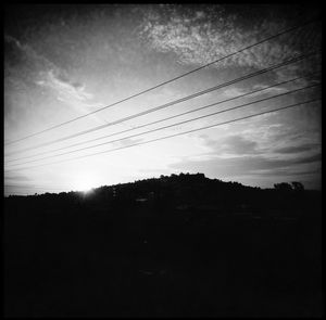 Silhouette trees and electricity pylon against sky