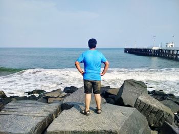 Rear view full length of man standing against sea on rock