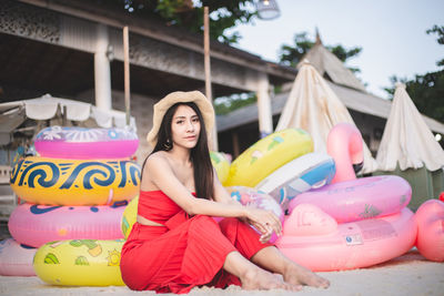 Portrait of young woman sitting by inflatable rings at shore of beach