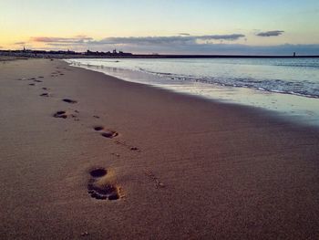 Footprints on sand at beach against sky during sunset