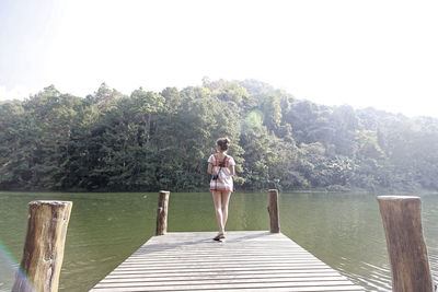 Woman standing on pier by lake against trees