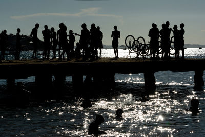 Dozens of young people, in silhouette, are seen on top of the crush bridge having fun. 
