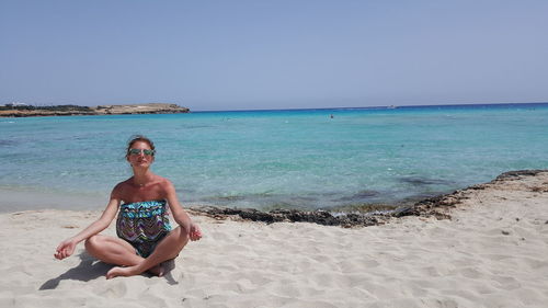 Portrait of smiling young woman on beach against clear sky