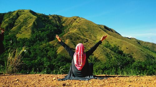 Rear view of woman with arms raised sitting against mountain