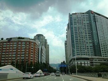 Cars on road by buildings against sky in city