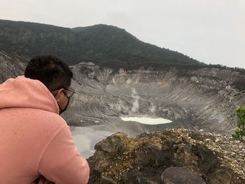 Rear view of man looking at rocky mountain against sky