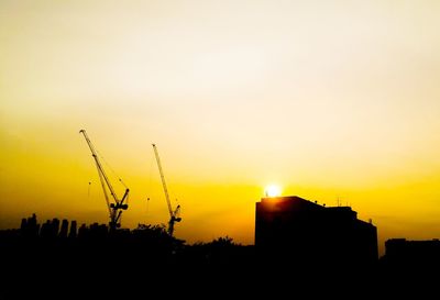 Silhouette cranes at construction site against sky during sunset