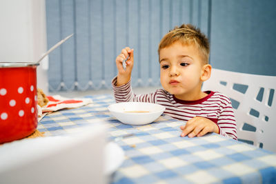 Cute boy eating food by table at home